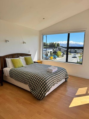 A bedroom with a large window, a bed with checkered bedding, and a view of a snowy mountain range.