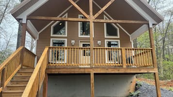 A two-story wooden cabin with a balcony, a staircase, and multiple windows.