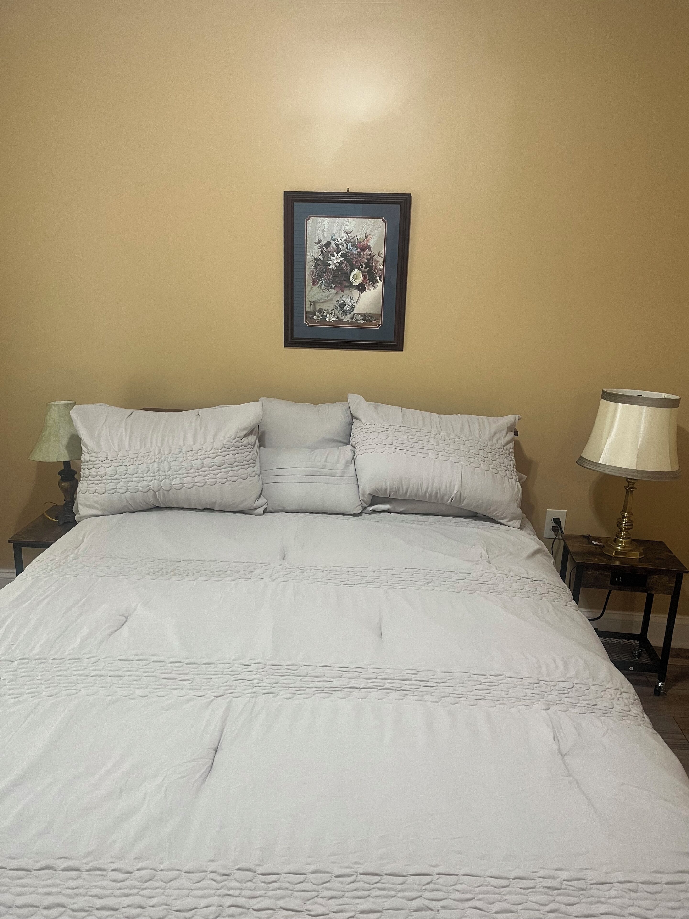 A bed with a white duvet and pillows, a framed picture on the wall, and two bedside lamps.