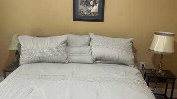 A bed with a white duvet and pillows, a framed picture on the wall, and two bedside lamps.