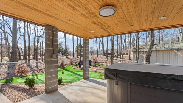 A covered patio with a hot tub, a view of a golf course, and a wooden ceiling.