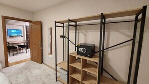 A room with a bed, a desk with a computer, a TV, and a storage unit with shelves.
