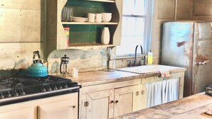 A rustic kitchen with a stove, sink, and wooden cabinets. - Charming historic cottage in Enoree (Enoree)