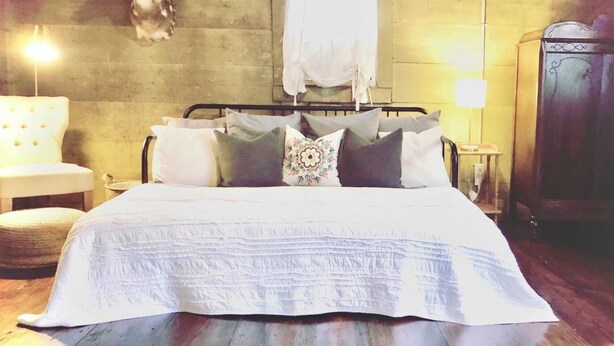A bedroom with a bed, pillows, a nightstand, a lamp, and a wooden floor. - Charming historic cottage in Enoree (Enoree)