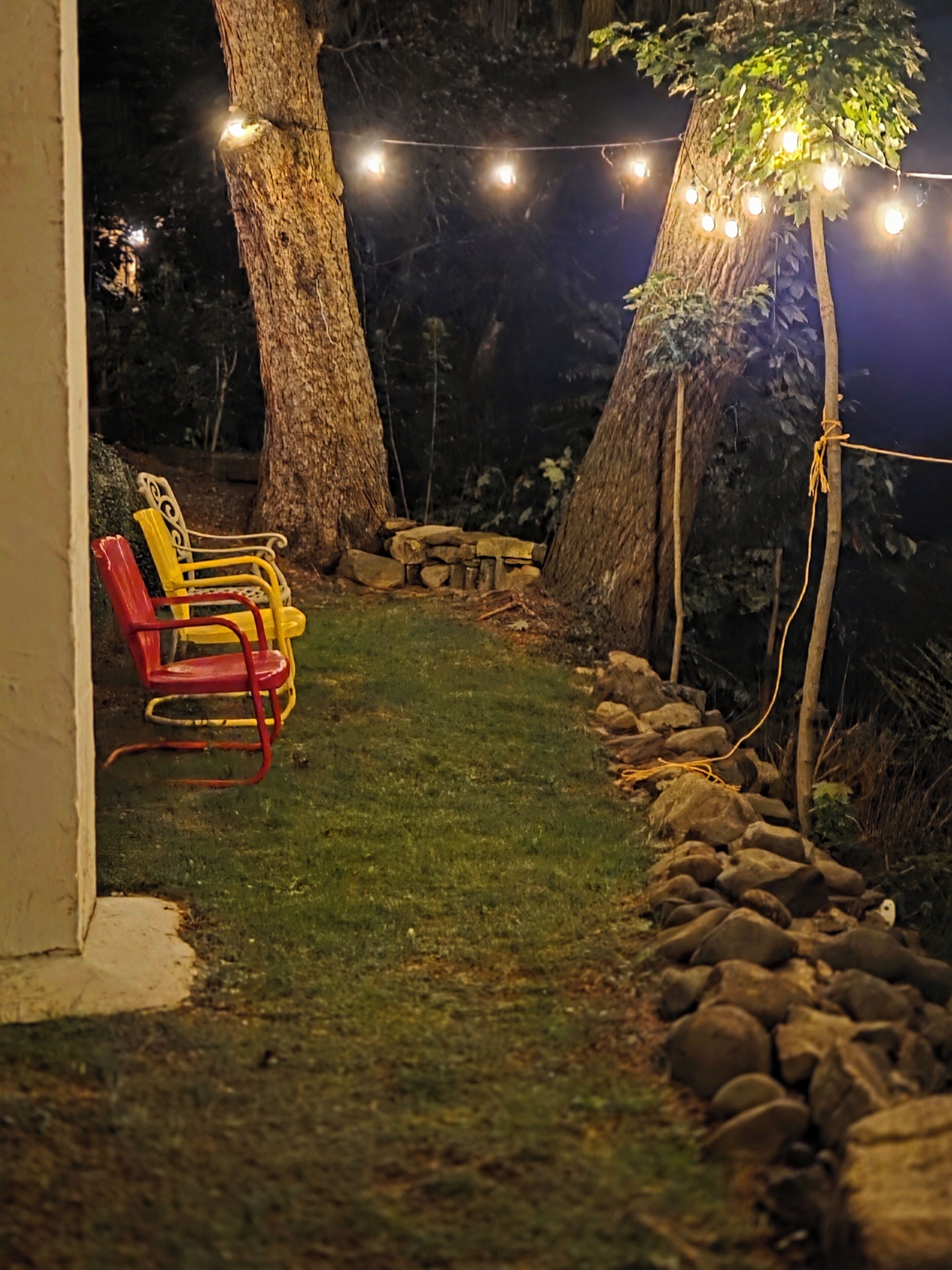 Ein Gartenbereich mit einer Steinmauer, einer Bank und Lichterketten.