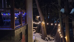 A snow-covered pathway leading to a building with a mural, string lights, and outdoor seating.