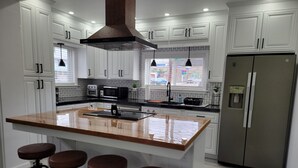 A modern kitchen with white cabinetry, a central island with stools, a stainless steel refrigerator, and pendant lighting.