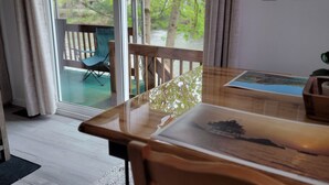 A room with a wooden table and chairs, a glass door leading to an outdoor area with a chair and a view of trees.