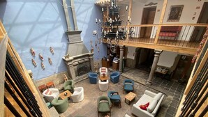 Un vaste espace salon doté de nombreux sièges, d’une cheminée et d’un lustre.