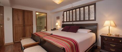 A bedroom with a large bed, two bedside tables, a wooden wardrobe, and a bench.