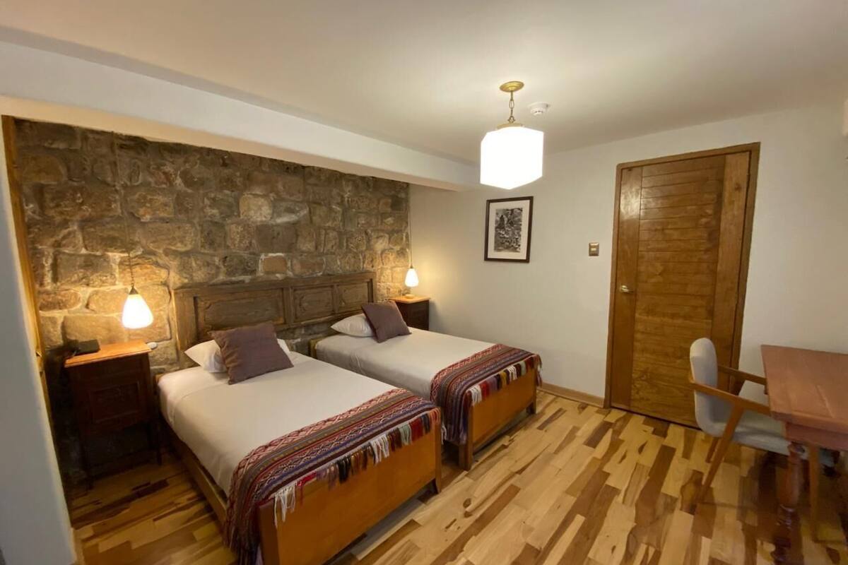 Una habitación con dos camas, una pared de piedra, una puerta de madera y una pequeña mesa con una silla.