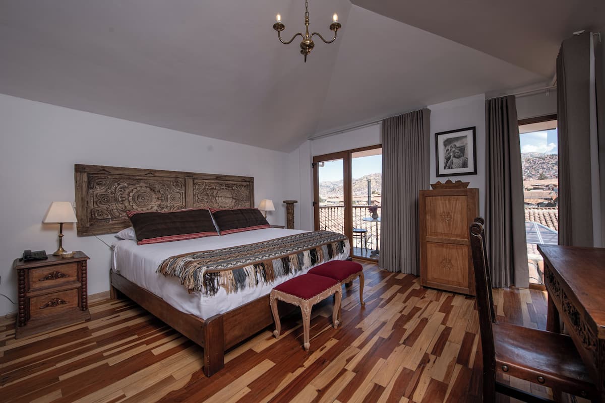 Un dormitorio con una cama grande, suelo de madera, un candelabro, un armario de madera y un balcón con vistas.
