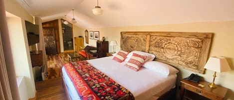 A bedroom with a large bed, a wooden headboard, a bedside table with a lamp, and a desk with a chair.