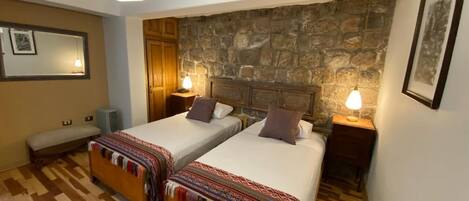 Una habitación con dos camas, una pared de piedra, suelo de madera y un banco.