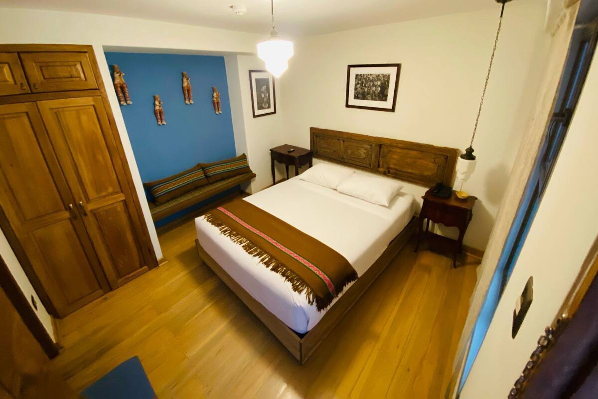 Un dormitorio con una cama de madera, un banco, un armario y una pared decorada con marcos.