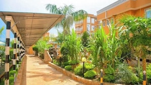 A covered walkway with a patterned floor, surrounded by lush greenery and palm trees. - Maya Holiday Point Kisii (Ogembo)