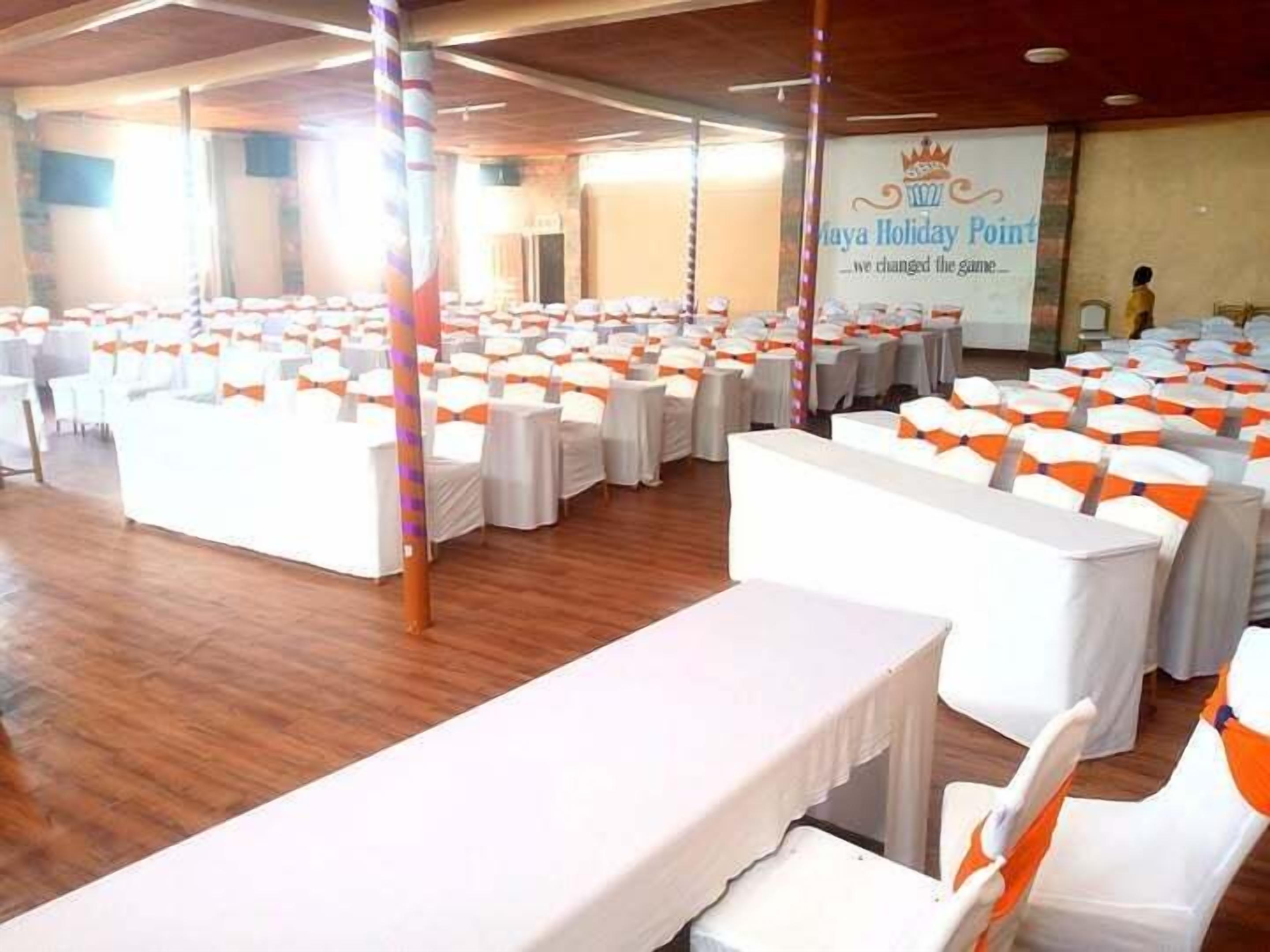 A banquet hall with rows of tables and chairs, a stage with a banner, and a wooden floor.