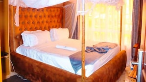 A bed with a canopy, a wooden headboard, and a bedside table with a lamp. - Maya Holiday Point Kisii (Ogembo)