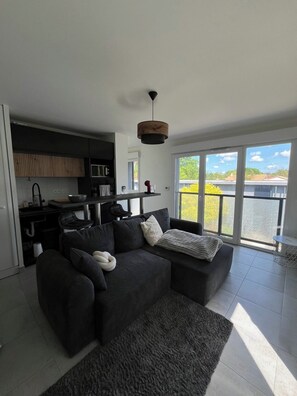 A modern living room with a dark sofa, a coffee table, and a view of a body of water through large windows.