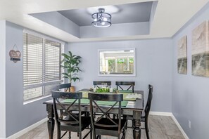 A dining area with a table set for four, surrounded by chairs, a potted plant, and a wall-mounted mirror. - Family friendly oasis 4 bedrm 2 bathrm 4 beds (Mesa)