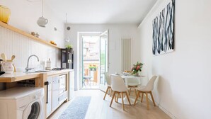 A modern kitchen with a built-in washing machine, a dining area with white chairs, and a view of the outside balcony. - COZY NEST IN THE HEART OF VERONA (Verona)