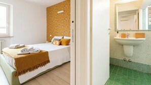 A bedroom with a bed, a bedside table, and a window. The room has a door leading to a bathroom with a sink and mirror. - COZY NEST IN THE HEART OF VERONA (Verona)