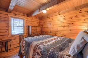 Ein gemütliches Blockhaus-Zimmer mit Bett, Fenster, kleinem Tisch und Holzschrank.