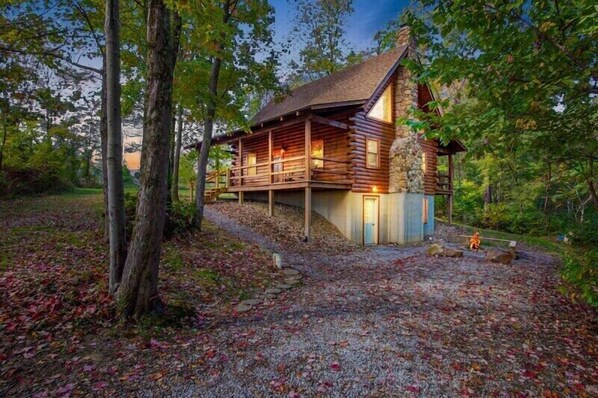 A log cabin with a stone foundation, wooden deck, and a stone fireplace.