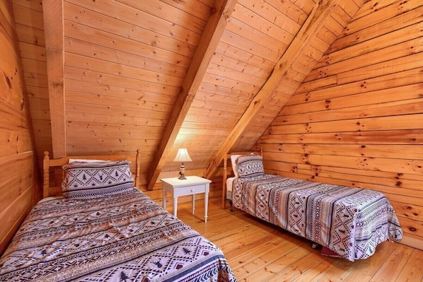 A cozy attic bedroom with two beds, wooden walls, and a small white nightstand. - Woods Edge Cabin | Hocking Hills, Hot Tub, Pets (Logan)