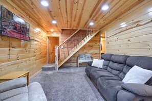 A cozy room with a wooden interior, a gray sofa, a small table, and a staircase leading to another area.