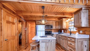 A wooden cabin-style kitchen with a central island, bar stools, a refrigerator, microwave, stove, and wooden cabinets.