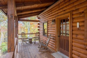 A log cabin with a porch, rocking chairs, and a wooden door with windows.
