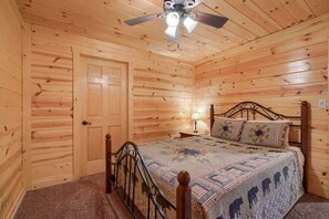 A wooden-paneled room with a bed, a ceiling fan, and a door.