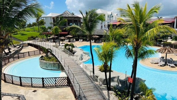 Een resort met een rond zwembad, een houten terras en palmbomen.