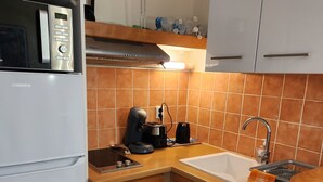 Een kleine keuken met een koelkast, magnetron, koffiezetapparaat, broodrooster en spoelbak.