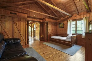 L’intérieur d’une cabane en bois, avec un lit, un canapé et une porte donnant sur une autre pièce.