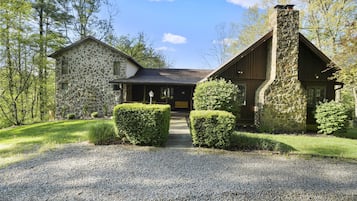 A stone house with a stone chimney, surrounded by a gravel driveway and trimmed hedges.
