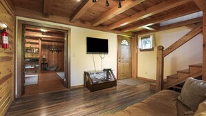 A wooden interior with a sofa, a TV mounted on the wall, and a staircase.