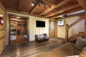 A wooden interior with a sofa, a TV mounted on the wall, and a staircase.