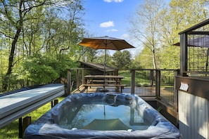 A hot tub with a wooden deck, a picnic table, and an umbrella.