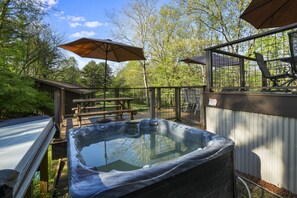 A hot tub with a wooden deck, picnic tables, and umbrellas.