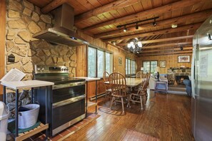 A rustic kitchen with stone walls, wooden ceiling, and a stone fireplace.