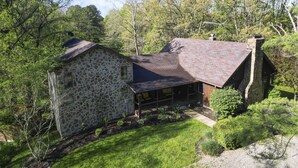 A stone house with a sloped roof, surrounded by a well-maintained lawn and dense trees.