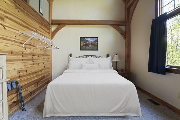 A bedroom with a wooden wall, a bed with white bedding, a picture on the wall, and a window with curtains.