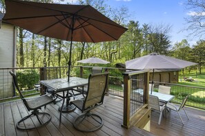 A wooden deck with a table and chairs, two umbrellas, and a small gazebo.
