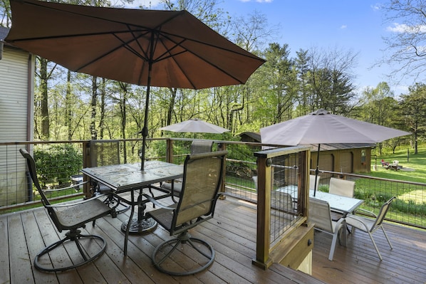 A wooden deck with a table and chairs, two umbrellas, and a small gazebo.