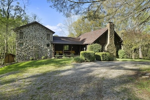 A stone and wood cabin with a gravel driveway, surrounded by trees and a well-maintained lawn.
