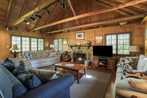 A cozy log cabin interior with a fireplace, wooden beams, a sofa, and a television.