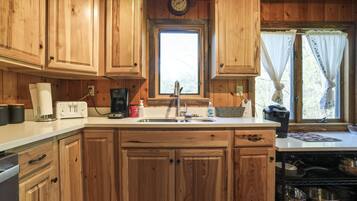 A wooden kitchen with a central island, a sink, and a window with curtains.
