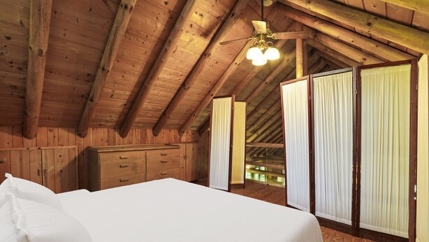 A wooden room with a bed, a dresser, and a ceiling fan.